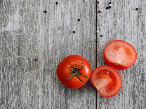 a picture of 2 tomatoes (1 picado ao meio) on a wooden surface as part of the Can rabbits eat tomatoes? Artigo do Bunnylowdown.
